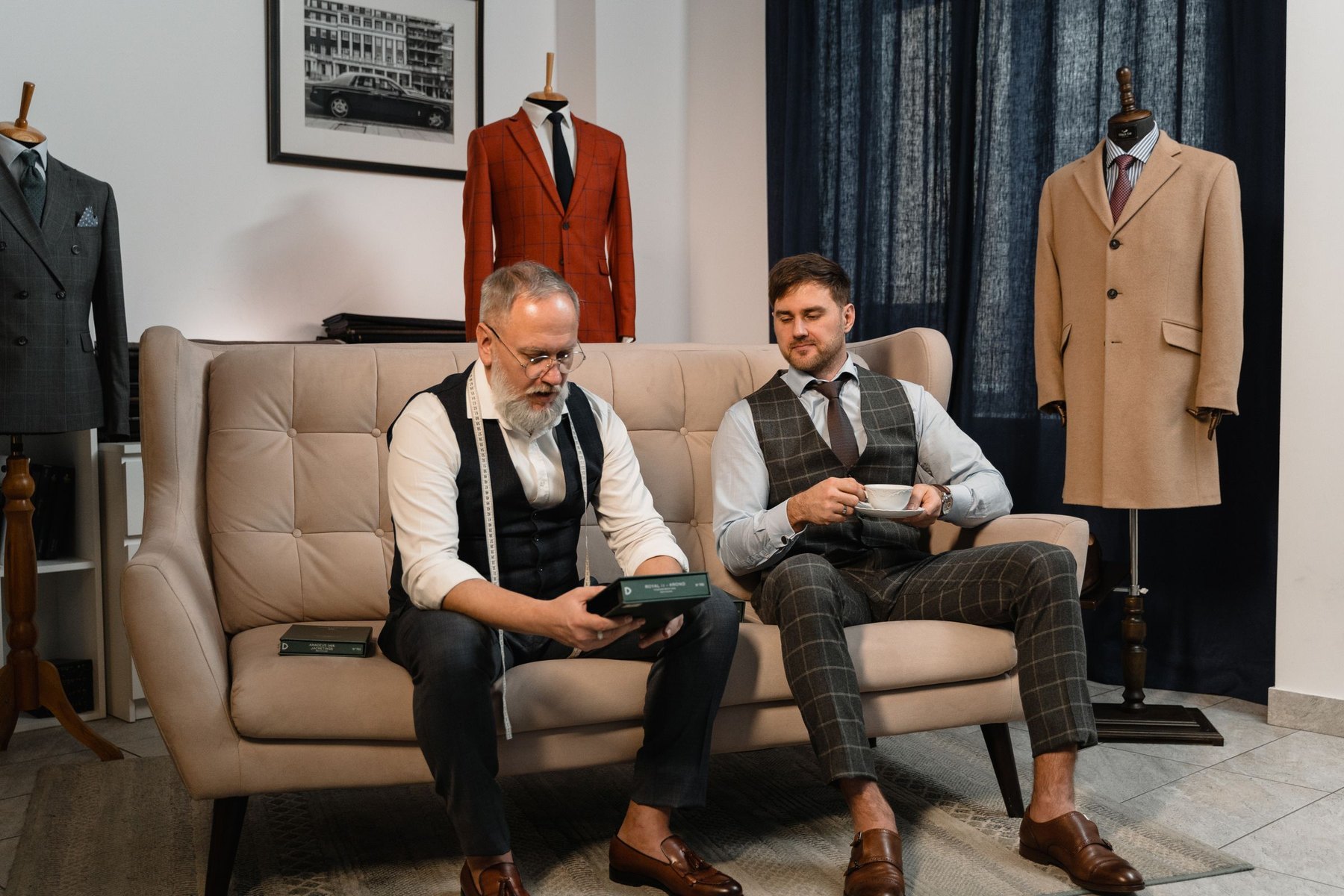 Two clients seated in the atelier with finished garments behind them
