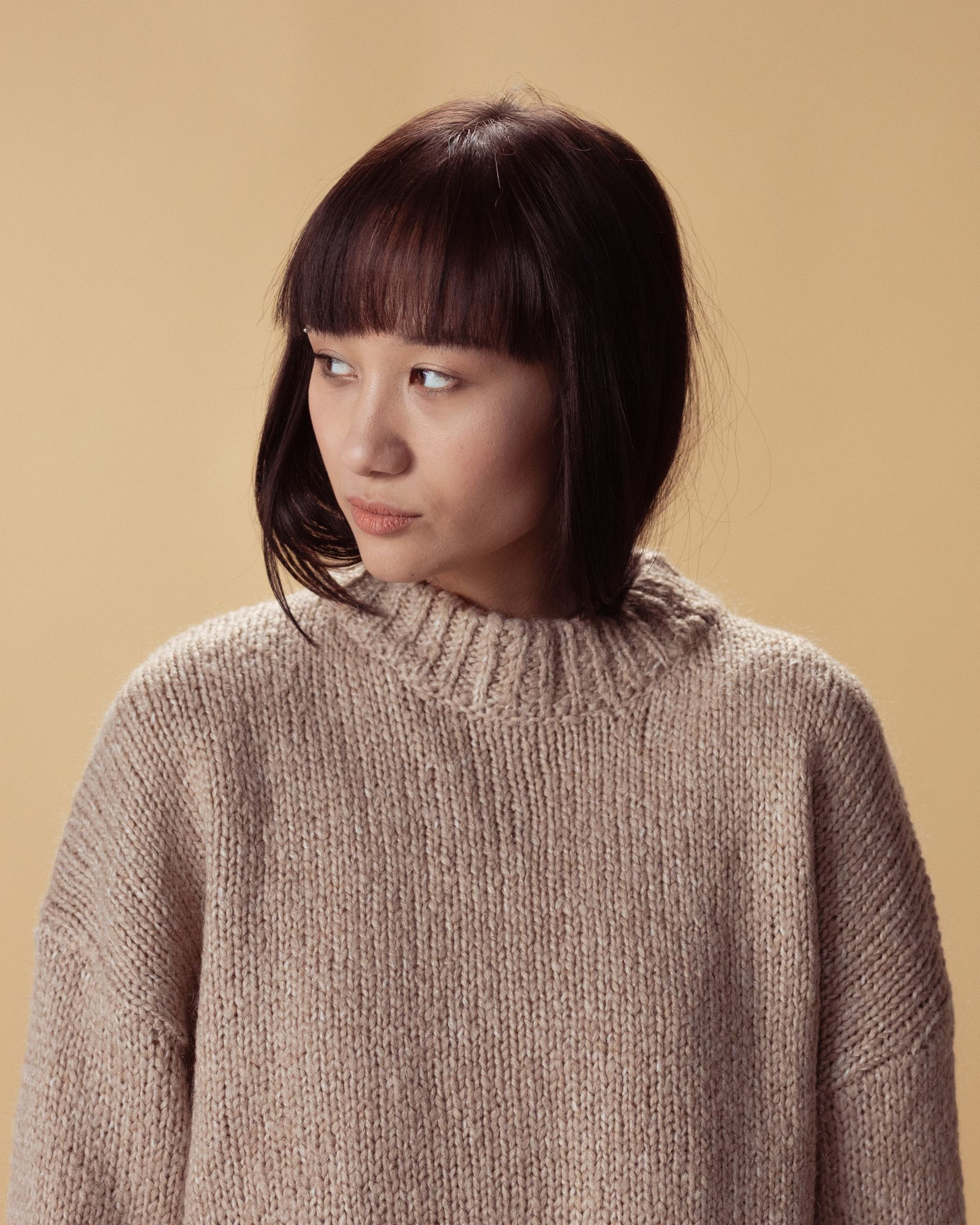 Woman wearing a hand-knitted camel roll-neck against a warm backdrop